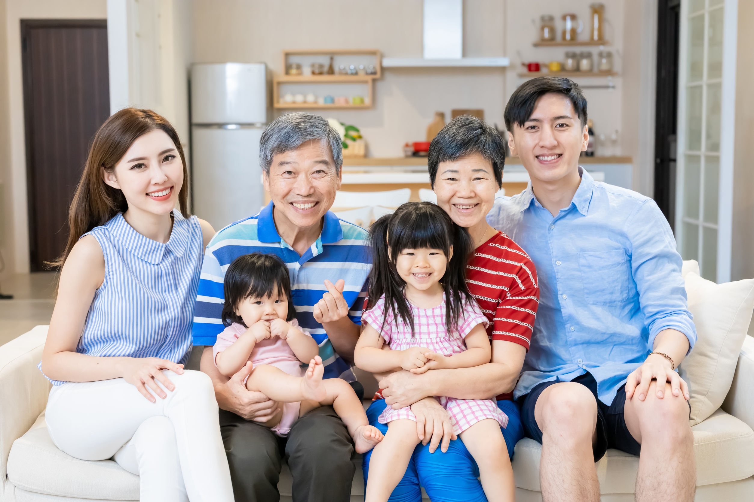 一對男女與他們的兩名女兒及父母坐在沙發上, 面帶笑容